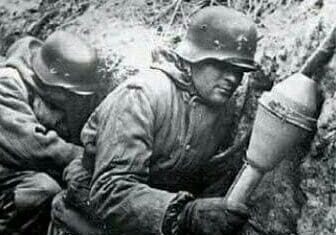 Two men in uniforms are working together on a trench.